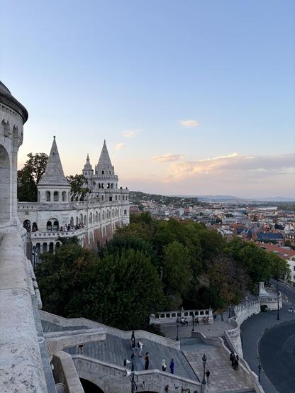 View of Fisherman's Bastion with its fairy-tale towers overlooking Budapest at sunset. People walk along the terraces and stairs.